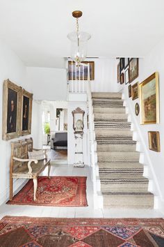 a staircase leading up to a living room with pictures on the wall and rugs