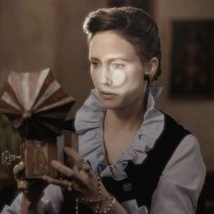 a woman holding a small wooden box in front of her face and wearing a blue dress