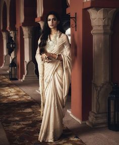 a woman in a white sari standing next to a wall with columns and pillars