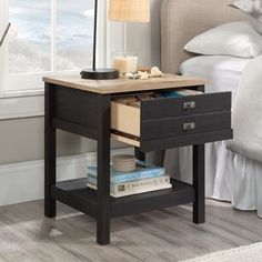 a night stand with two drawers and a lamp on the end table in front of a bed