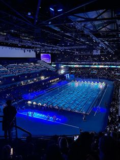 an indoor swimming pool is lit up with blue lights and people are standing on the sidelines