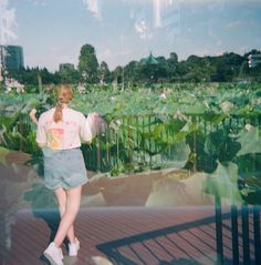 a woman walking across a bridge next to green plants