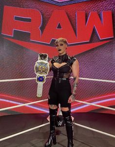 a woman holding a wrestling belt in front of a large sign with the word raw on it