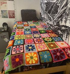 a bed covered in a multicolored blanket next to a wooden dresser and potted plant