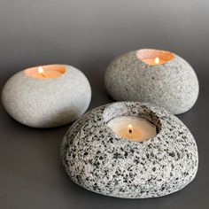 two rocks with lit candles in them sitting on a gray surface, next to each other