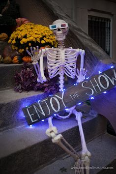 a skeleton holding a sign that says enjoy the show on it's front steps