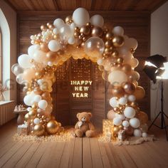 a teddy bear is sitting in front of an arch made out of gold and white balloons