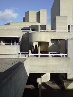 two people are standing on the balcony of a large building with concrete walls and balconies