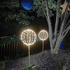 two decorative lights are lit up in the yard at night, near a tree and fence