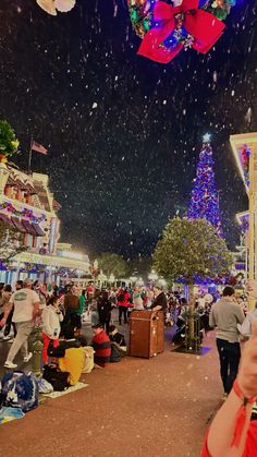 a crowd of people standing around a christmas tree in the middle of a town at night