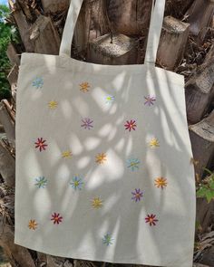 a white tote bag with multicolored flowers on it hanging from a tree