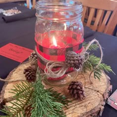 a glass jar filled with red candles sitting on top of a wooden table next to pine cones