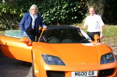 two people standing next to an orange sports car