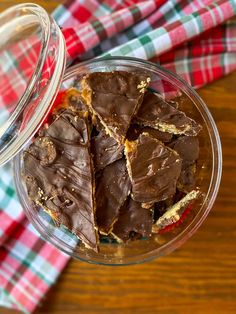 a glass bowl filled with pieces of chocolate on top of a wooden table next to a red and white checkered napkin