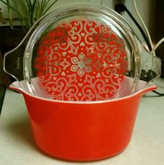 a red pot with an ornate design on the bottom and lid sitting on a counter