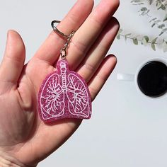 a hand holding a pink heart shaped keychain next to a cup of coffee