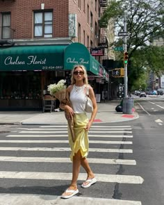 a woman is crossing the street with flowers in her hand and she is wearing sandals