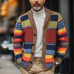 a man with a beard wearing a multicolored cardigan sweater and khaki pants