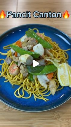 a blue plate topped with pasta and veggies on top of a wooden table