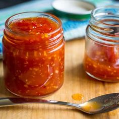 two jars filled with food sitting on top of a wooden table next to a spoon