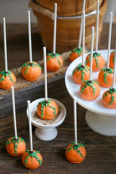 orange cake pops with green sprinkles are on a white plate next to a wooden tray