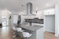 a large kitchen with white cabinets and stainless steel counter tops, along with bar stools