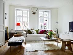 a living room filled with furniture and a white couch in front of two large windows