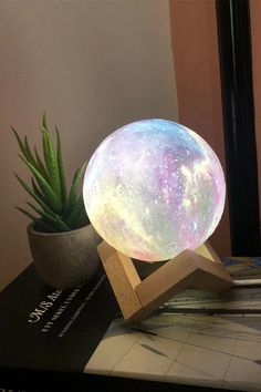 the moon lamp is sitting on top of a table next to a potted plant