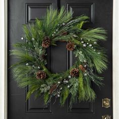 a wreath on the front door with pine cones and greenery hanging from it's side