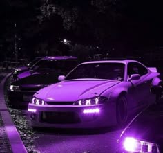 two cars are parked on the side of the road at night with purple lights in front of them