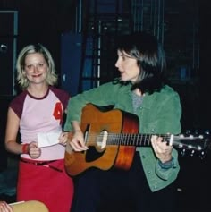 two women standing next to each other with guitars in their hands and one playing the guitar