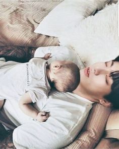 a young man laying on top of a bed next to a baby in his arms