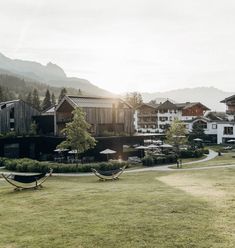 hammocks are in the grass next to some buildings and trees with mountains in the background