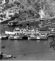 black and white photograph of boats docked in the water next to a mountain side town