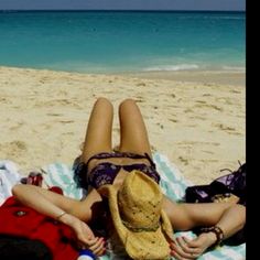 a woman laying on top of a beach next to a red teddy bear wearing a hat