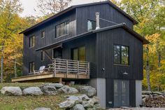 a black house in the woods surrounded by rocks and trees with fall foliage around it