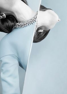 a woman in a blue dress is looking at herself in the mirror while wearing a diamond necklace