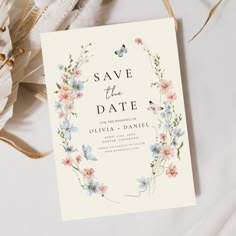 save the date card with flowers on it next to some feathers and other things that are laying around