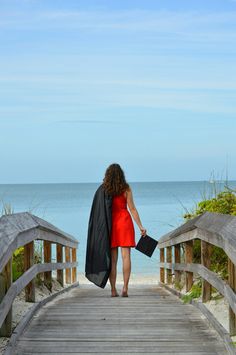 a woman in a red dress is walking across a wooden bridge towards the ocean and beach