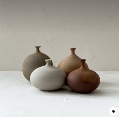 three ceramic vases sitting next to each other on a white counter top with a wall in the background