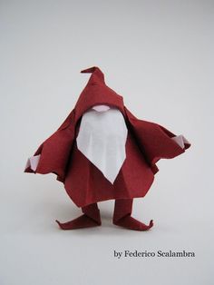 an origami santa claus is standing on one leg and wearing a red cape