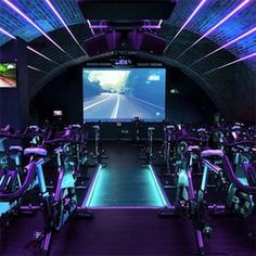 an indoor gym with rows of exercise bikes and large screen on the wall behind it