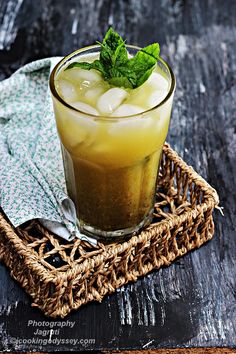 a glass filled with ice and mint sitting on top of a woven basket next to a napkin