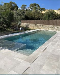 an empty swimming pool in the middle of a backyard with stone walls and trees around it