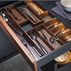 an open drawer with utensils and silverware in it on a black table