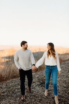 an engaged couple holding hands and walking through the woods