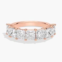 a rose gold ring with four princess cut diamonds on the sides and three smaller princess cut stones