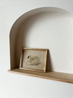 an empty shelf with a framed picture on it next to a white wall and wooden shelves