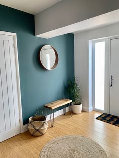 a living room with blue walls and wooden flooring is pictured in this image, there is a round mirror on the wall