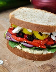 a close up of a sandwich on a cutting board with tomatoes, onions, peppers and lettuce